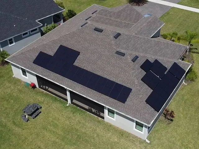 Aerial view of a dark shingle roof with a black solar panel array