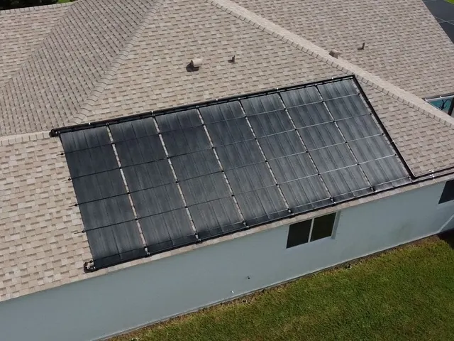 Aerial view of black pool heating collectors on a grey shingle roof