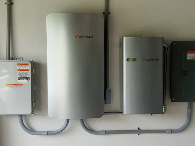 Two home battery units and electrical panels mounted on a garage wall