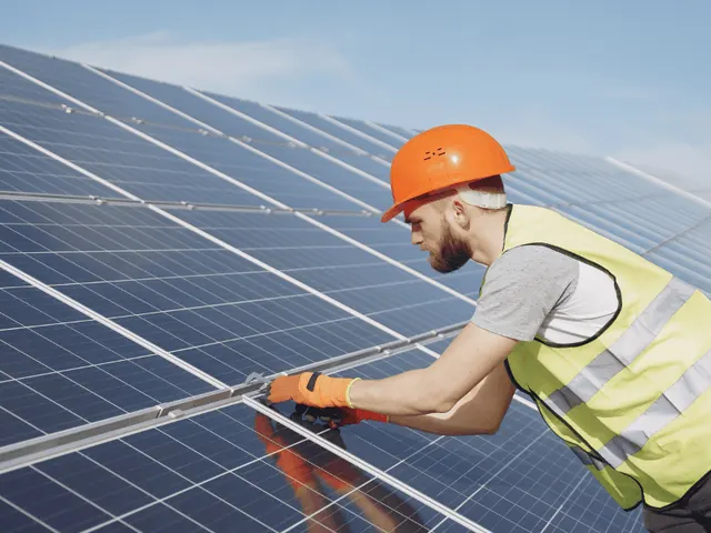 Installer in an orange hard hat and hi-vis vest fitting a solar panel