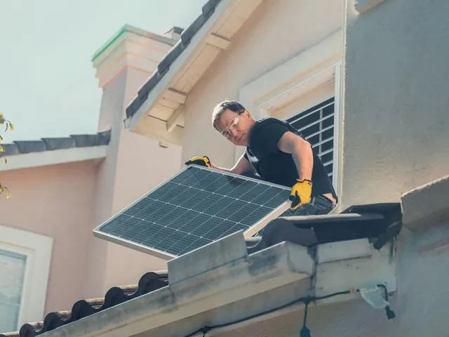 Installer carrying a solar panel down from a pitched roof near a window