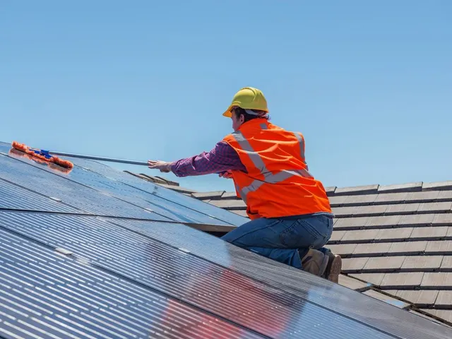 Installer in an orange vest and hard hat working on solar panels on a roof