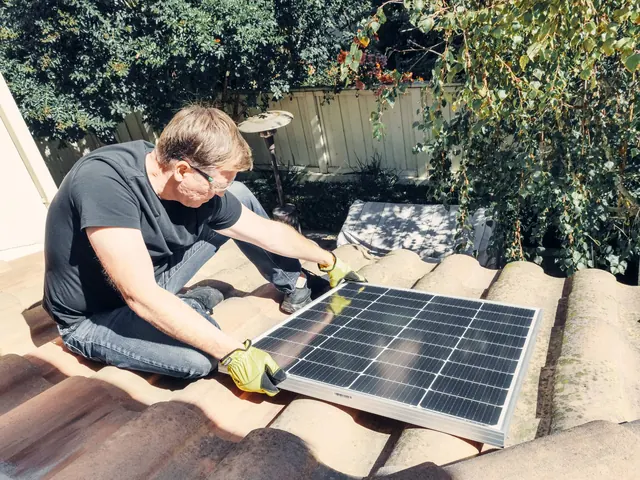 Installer lifting a solar panel off a terracotta tile roof