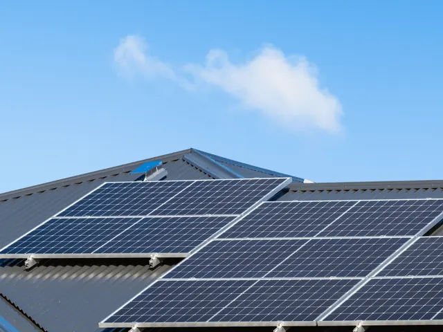 Solar panels on a roof under a blue sky with a single cloud