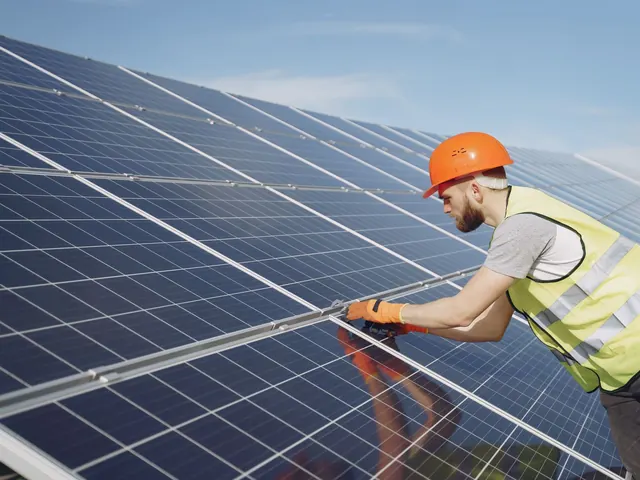 Technician in a hard hat fastening a solar panel on a sunny roof