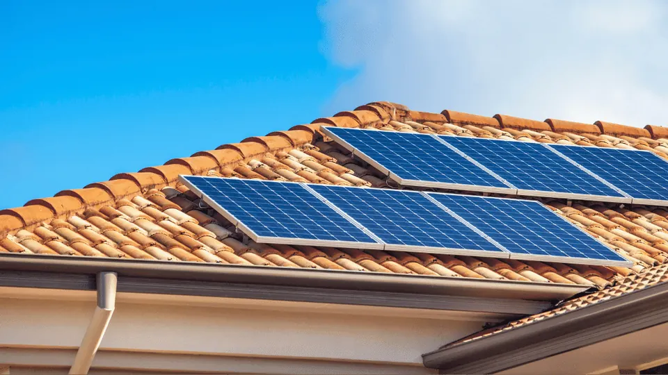 Blue solar panels on a terracotta tile roof under a clear sky